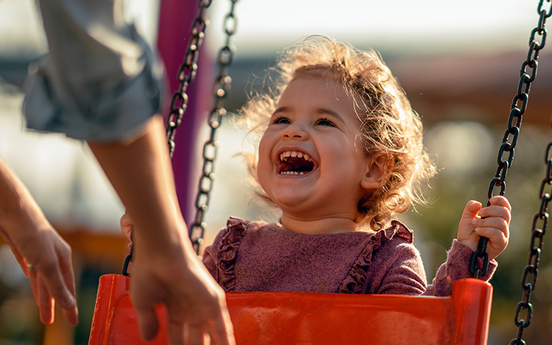 A toddler laughing as they are being pushed on a swing.